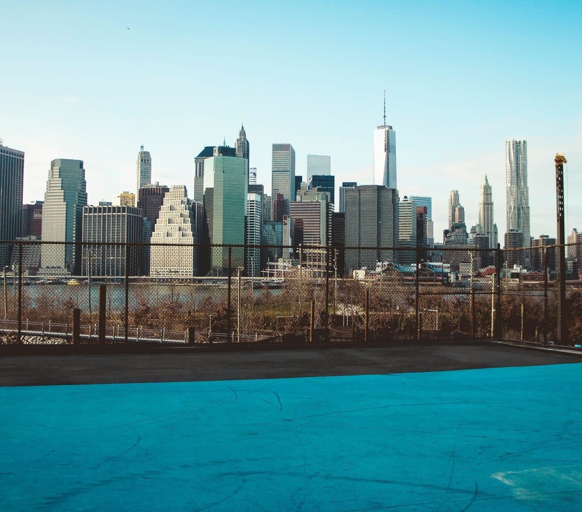 The Lower Manhattan skyline rising behind a blue public tennis court
