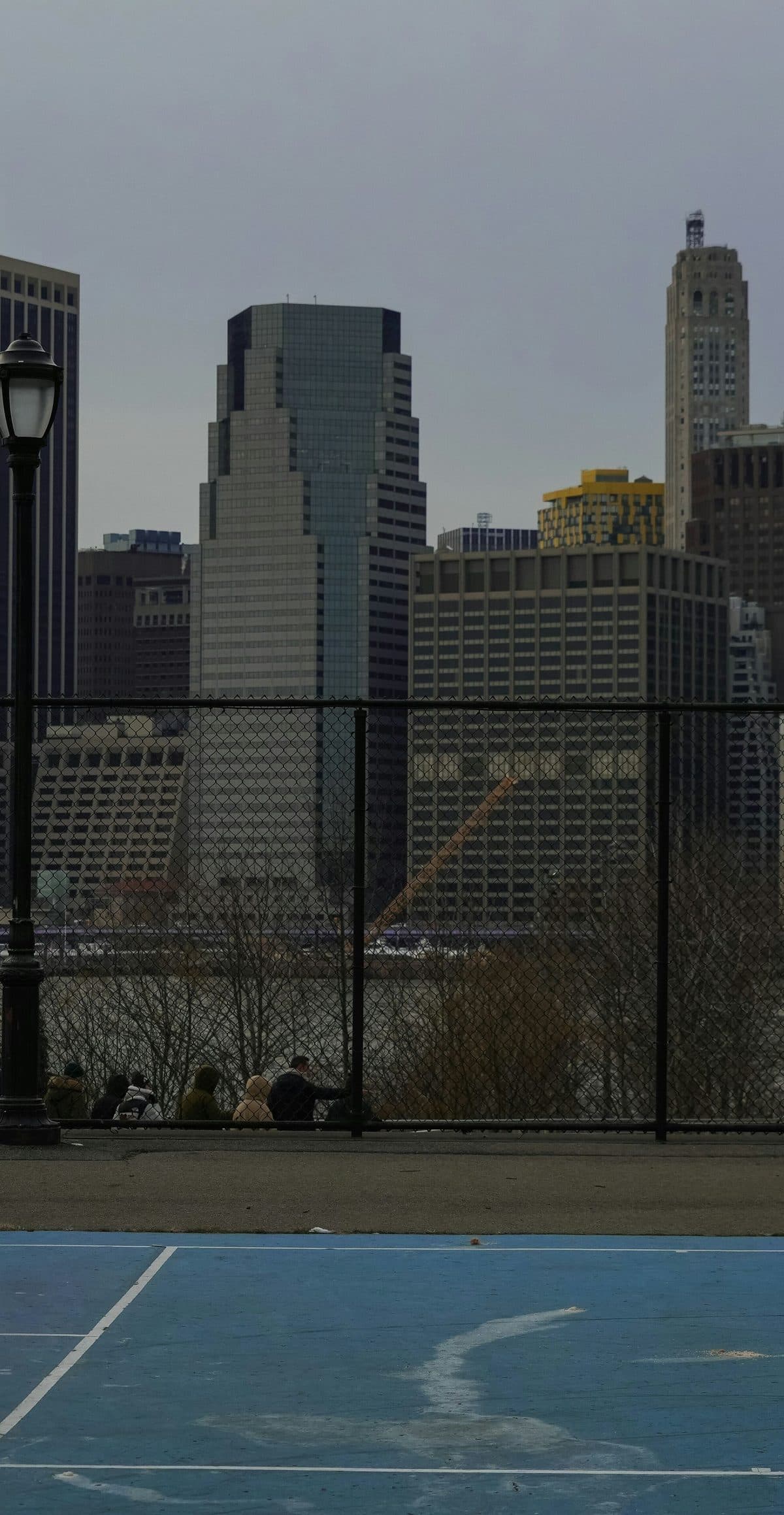 A blue public tennis court on the water with the Manhattan skyline behind